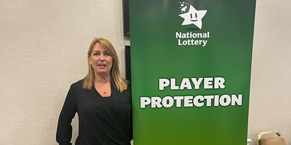 Susan Lawson is wearing a black top while standing beside a pull-up banner with the words Player Protection on it